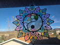 Metal and resin yin-yang mandala suncatcher with lavender, pink, aqua and yellow petals hanging in a window, front view