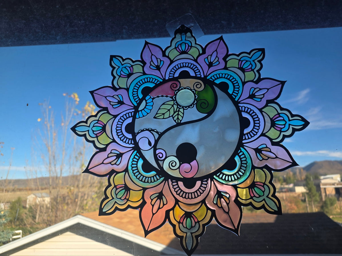 Metal and resin yin-yang mandala suncatcher with lavender, pink, aqua and yellow petals hanging in a window, front view