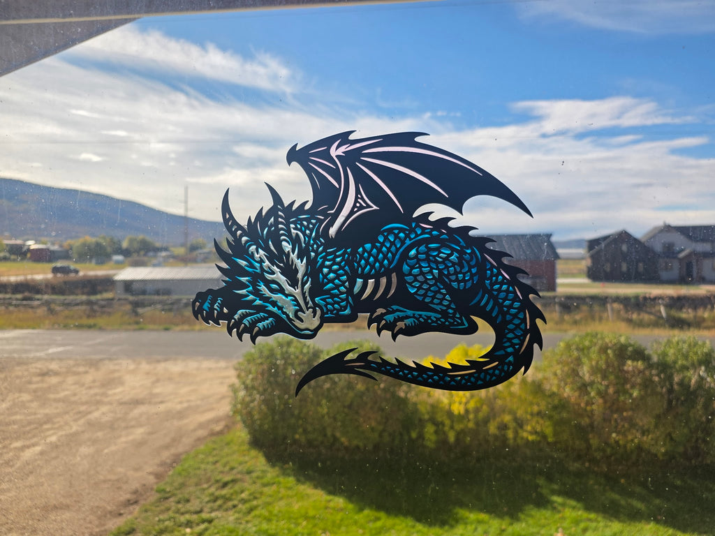 Sleeping dragon epoxy resin window art in metallic blue displayed in a window with a mountain view